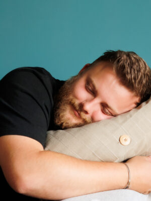 junger Mann mit Bart kuschelt sich auf ein Kissen bei Armlehne eines Sofa und lächelt zufrieden